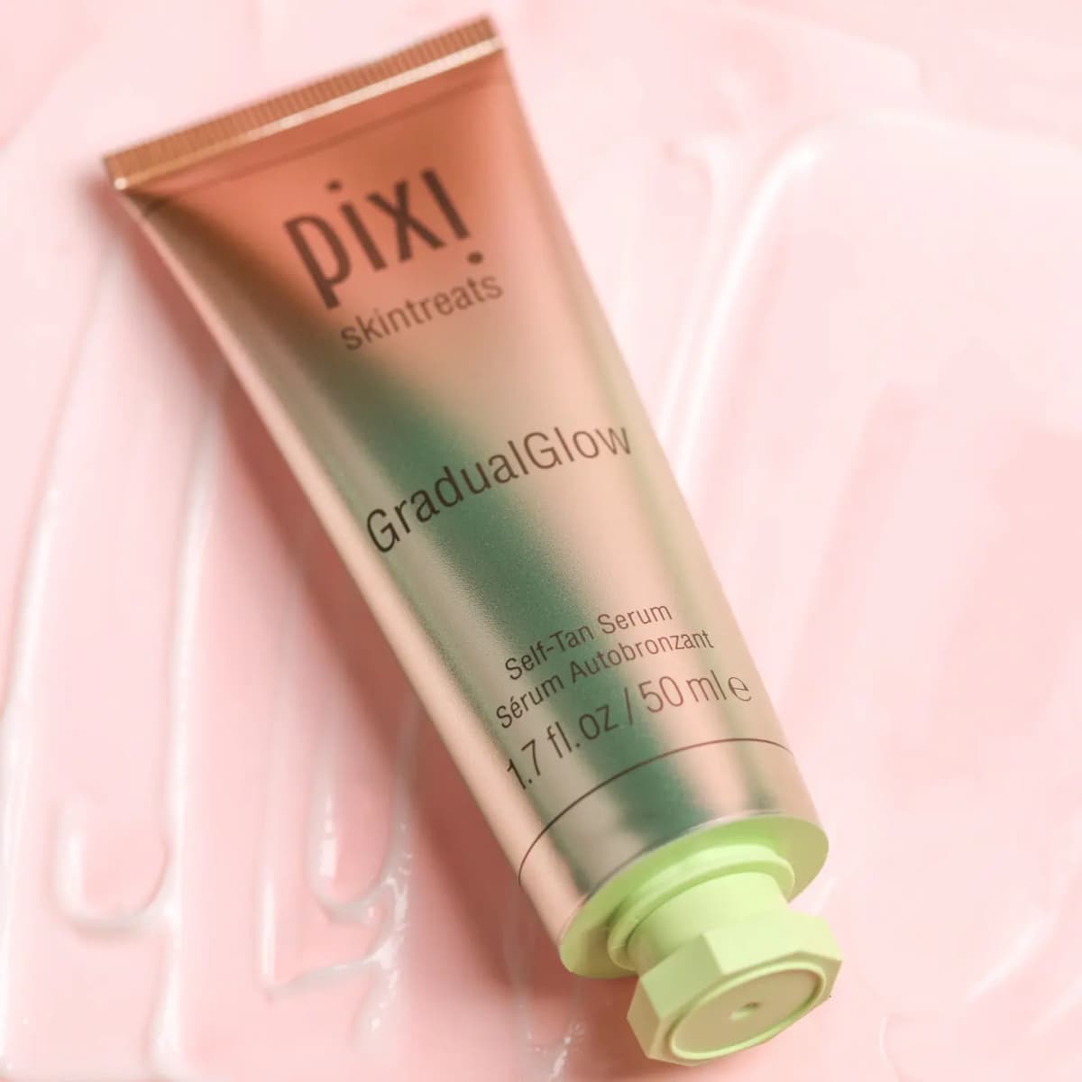 Pixi GradualGlow Self-Tan Serum, 50 ml rose-gold and green tube lying on a pink creamy swatch