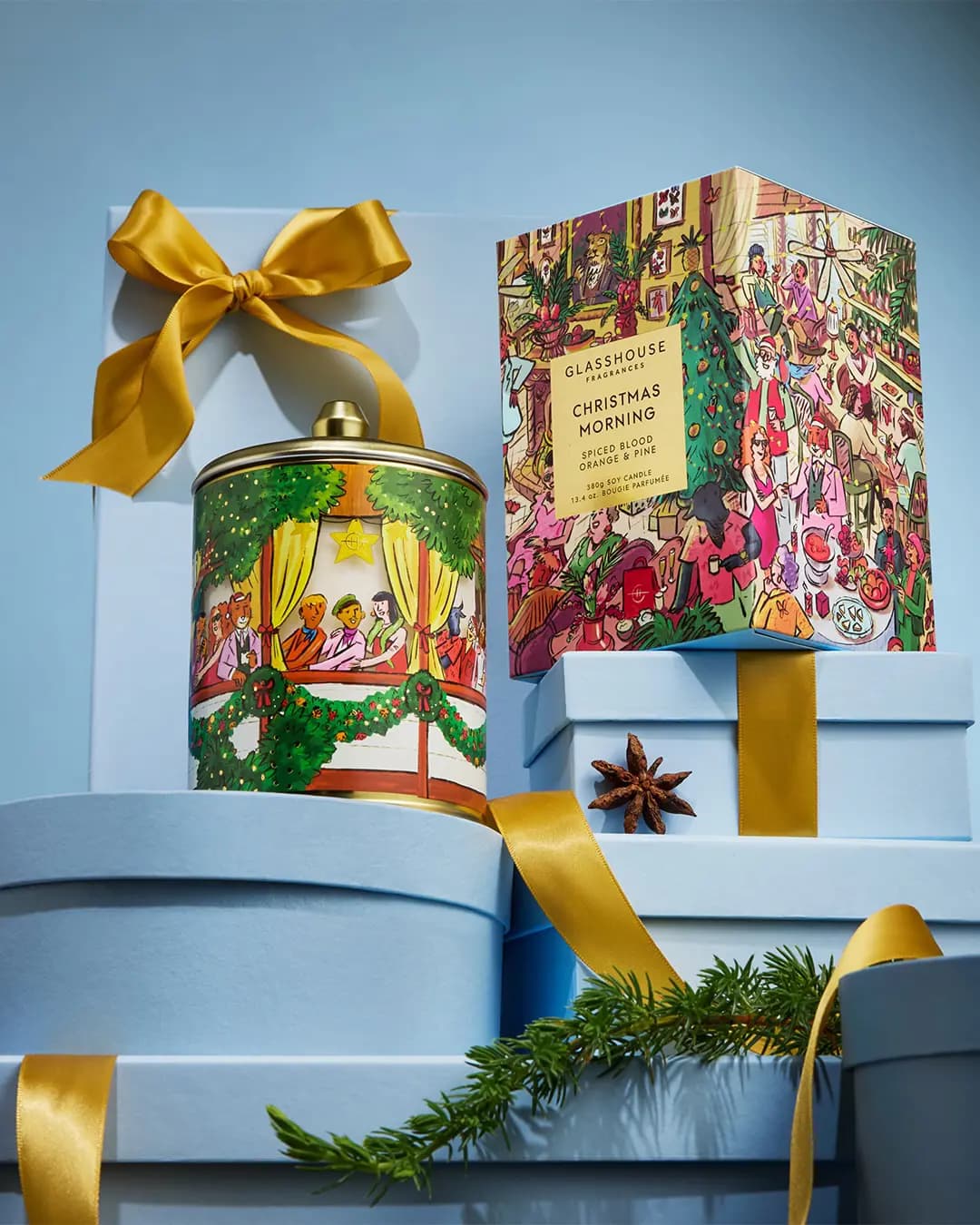 Glasshouse Christmas Morning candle in a gold-lidded tin beside its box on pale blue gift boxes with gold ribbon