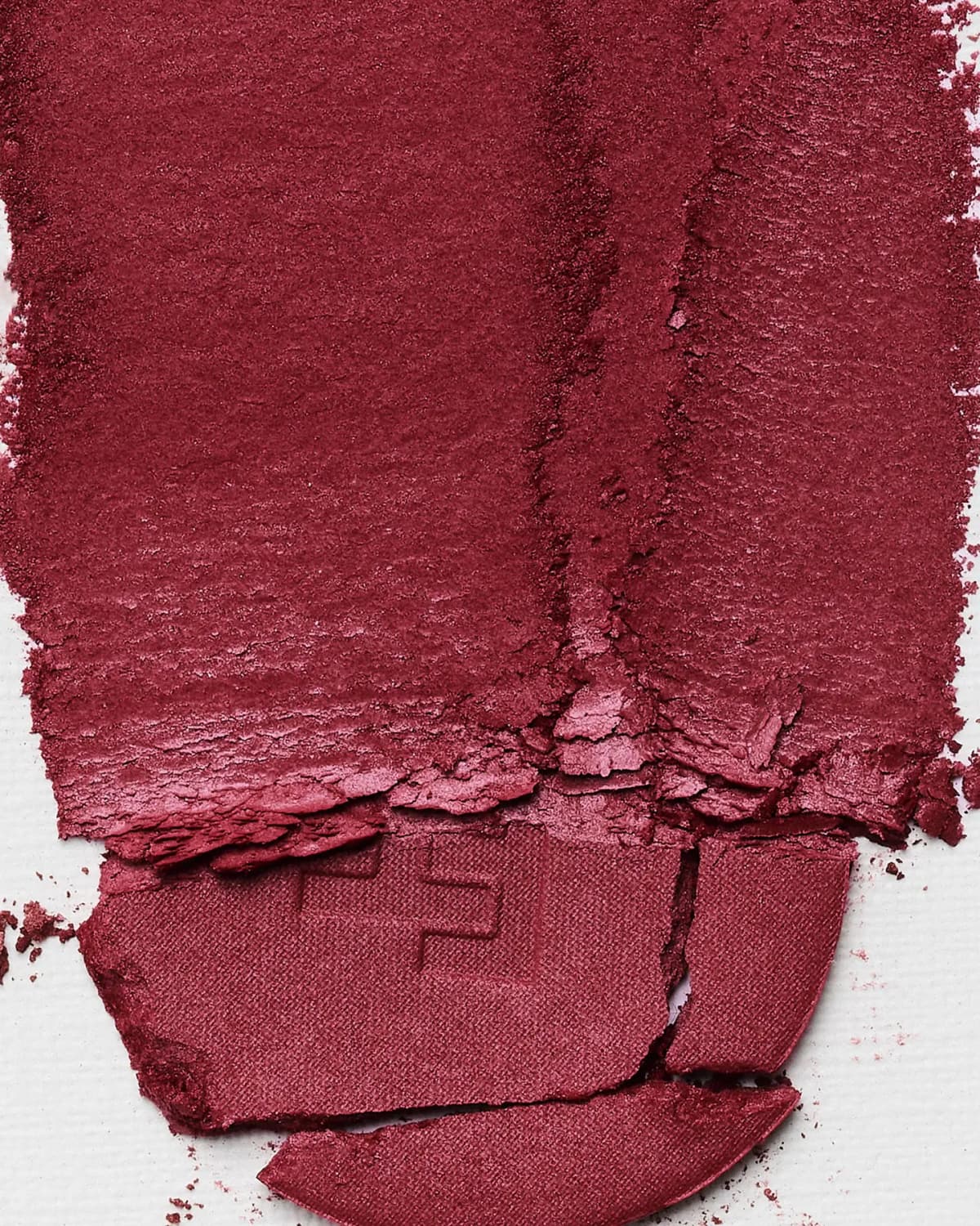 Deep burnished-berry powder swatch with a broken FH-embossed pan fragment on white textured paper