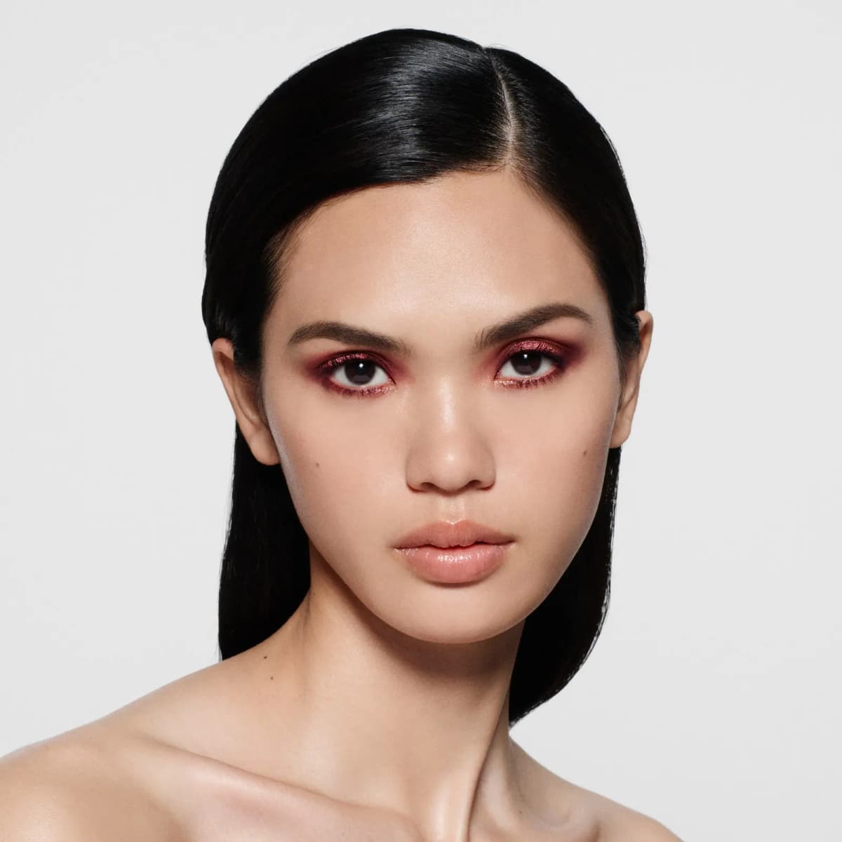 Model with sleek black hair wearing shimmery burgundy-copper eyeshadow and plum liner along the lower lash line