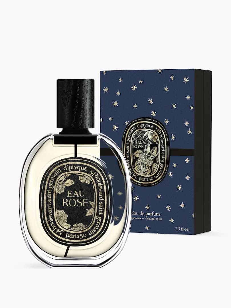 Eau Rose bottle with gold-engraved rose label in front of its starry navy gift box