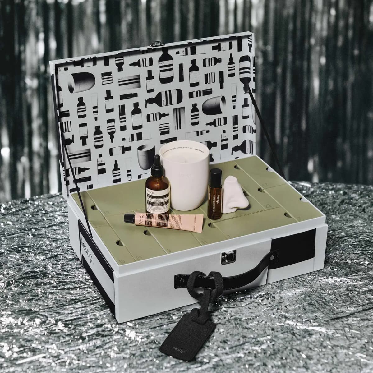 Open Aesop suitcase calendar showing green numbered drawers with candle, serum, hand balm and ceramic nose on top.