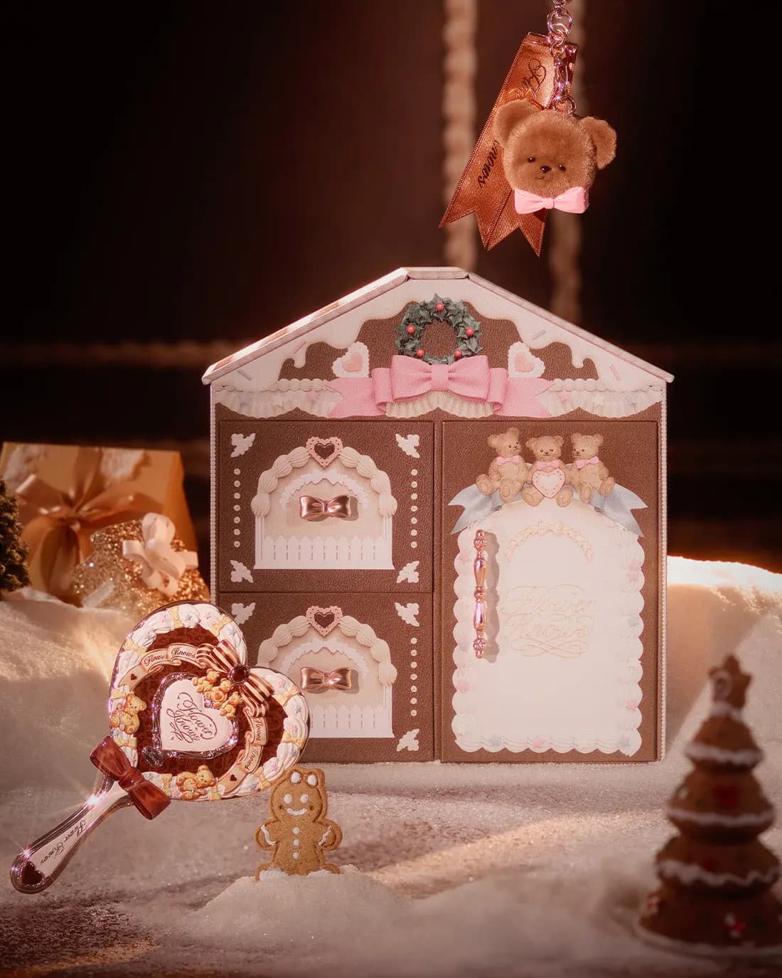 Brown house box with wreath, pink bow and three teddy bears, beside a heart hand mirror and gingerbread cookie