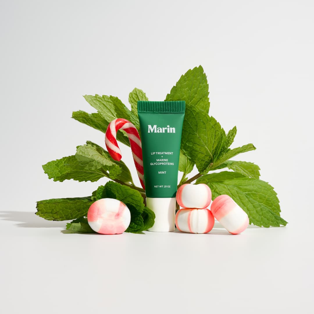 Green Mint tube against fresh mint leaves, a candy cane and pink-striped mints