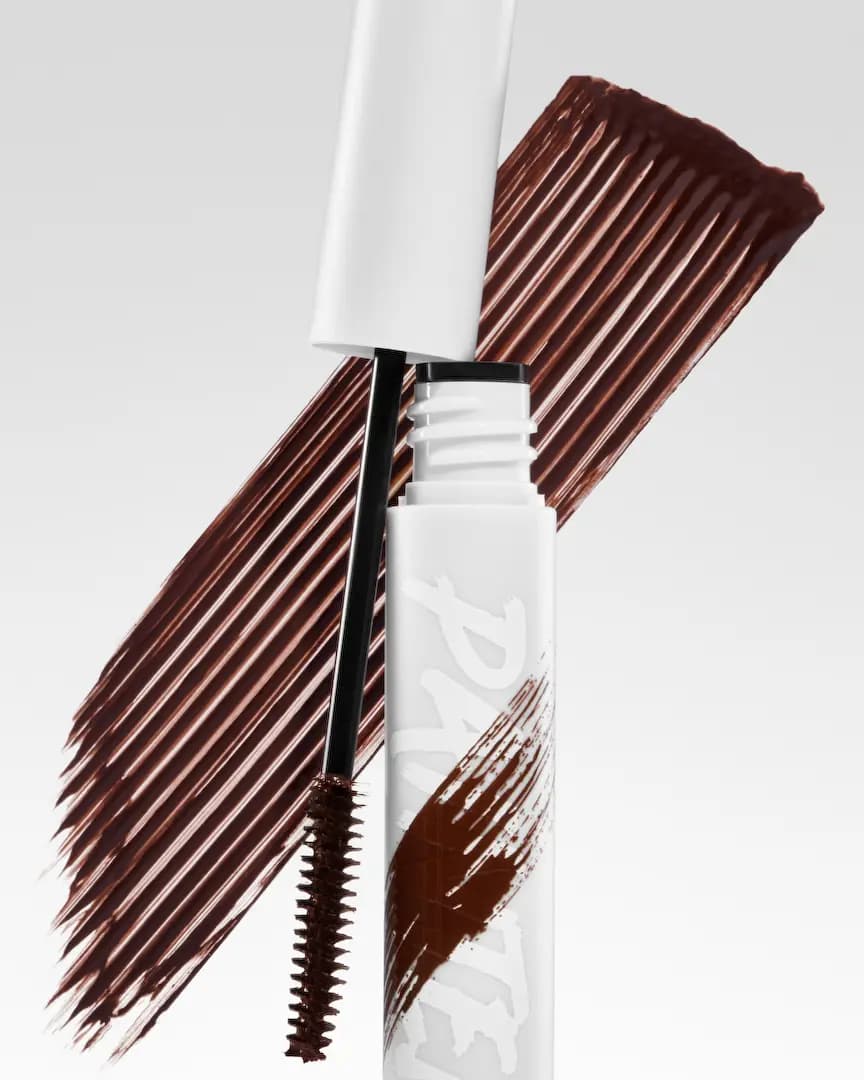 Open tube with brown-coated spoolie wand in front of a broad brown mascara swatch