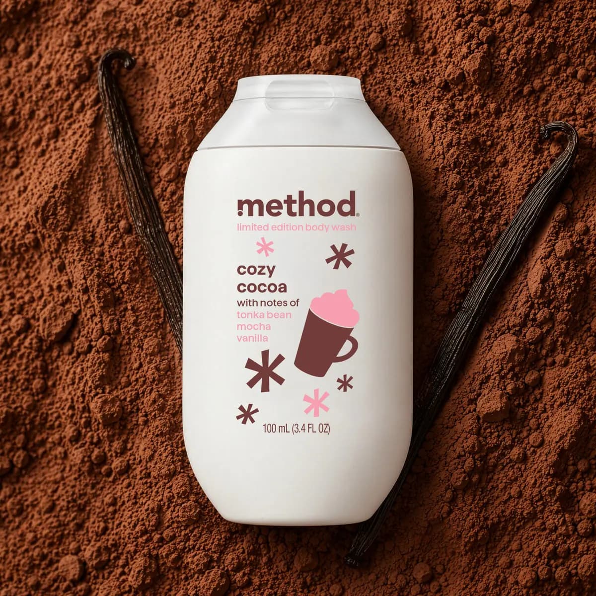 Cozy Cocoa body wash bottle lying on cocoa powder between two dark vanilla bean pods