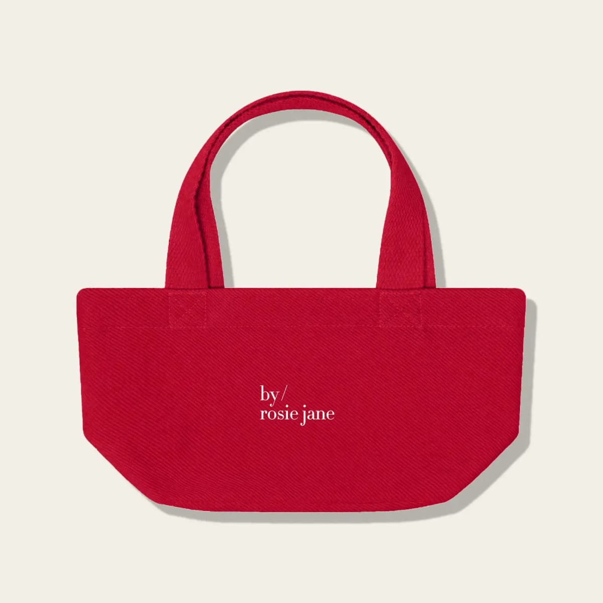 Small red twill tote bag with short handles and white by/rosie jane logo on a cream background