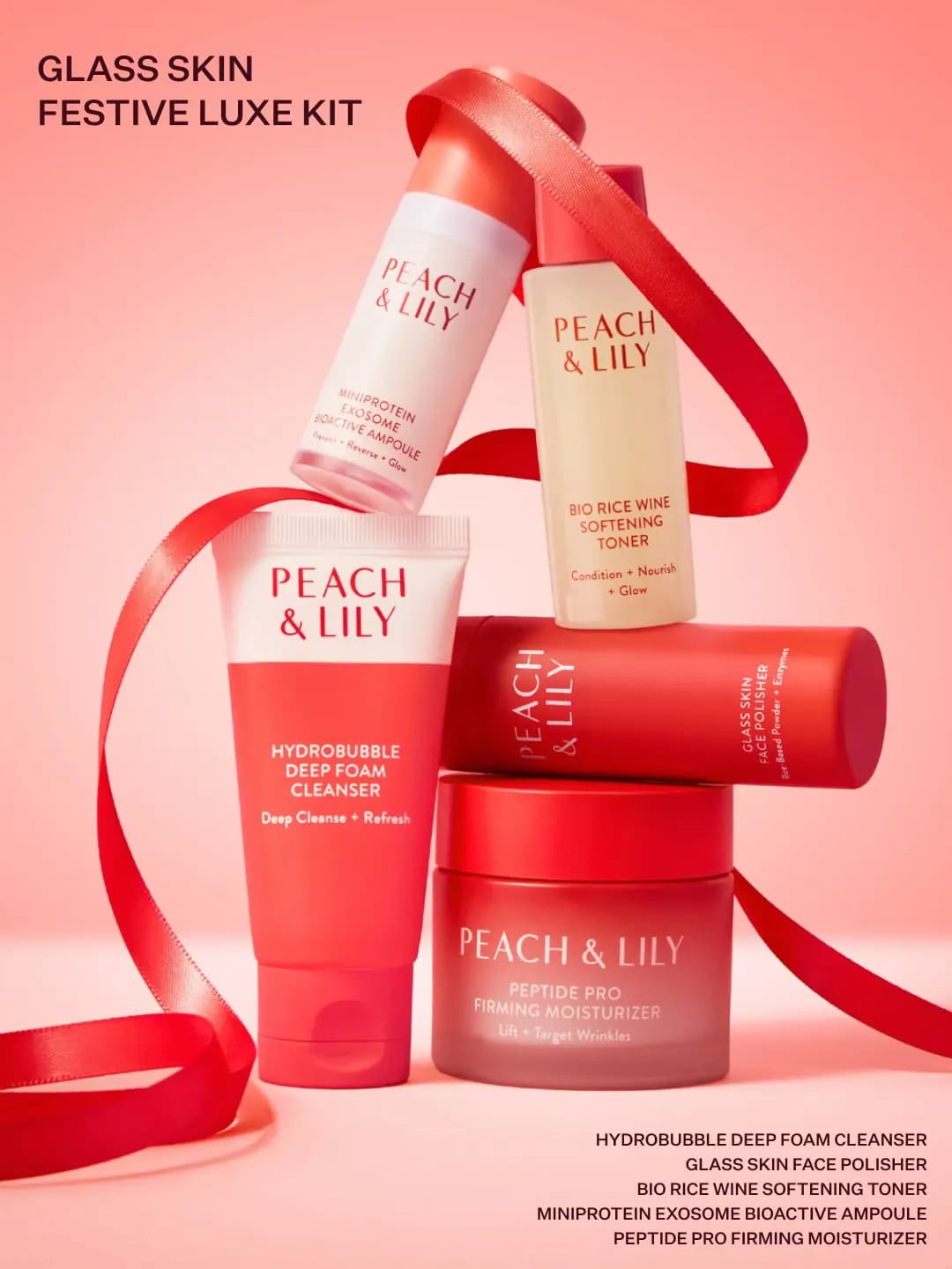 Five Glass Skin Festive Luxe Kit products balanced in a stack, wrapped with red ribbon on a peach background