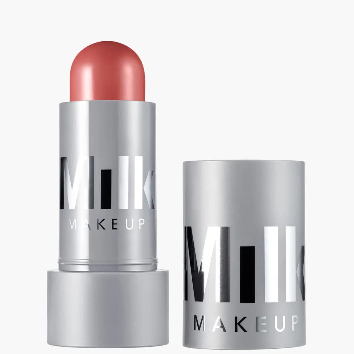 Open grey MILK MAKEUP cream stick with a domed dusty rose bullet, its cap standing beside it