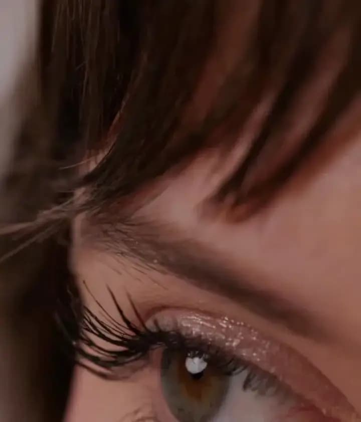 Close-up of a hazel eye with long lashes and a sparkly pink-champagne glitter wash on the lid