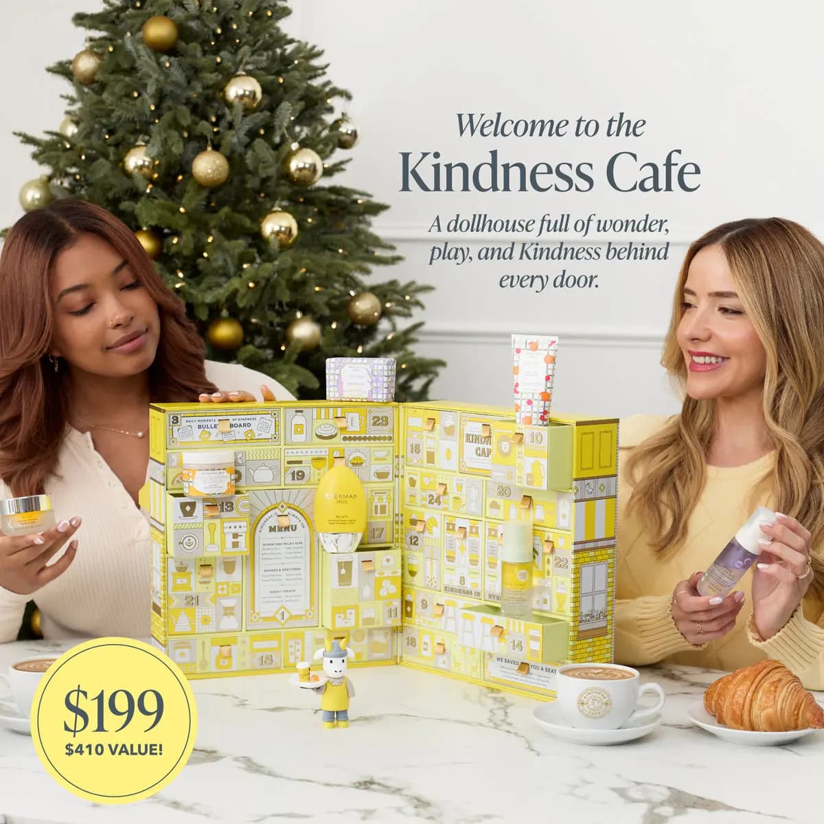 Two people at a marble table with the open Kindness Cafe advent calendar, holiday tree behind, $199 and $410 value badge