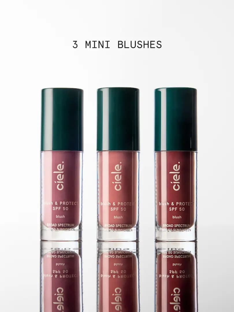 Three mini blush & PROTECT SPF 50 bottles in mauve, pink and brick shades with green caps, reflected below