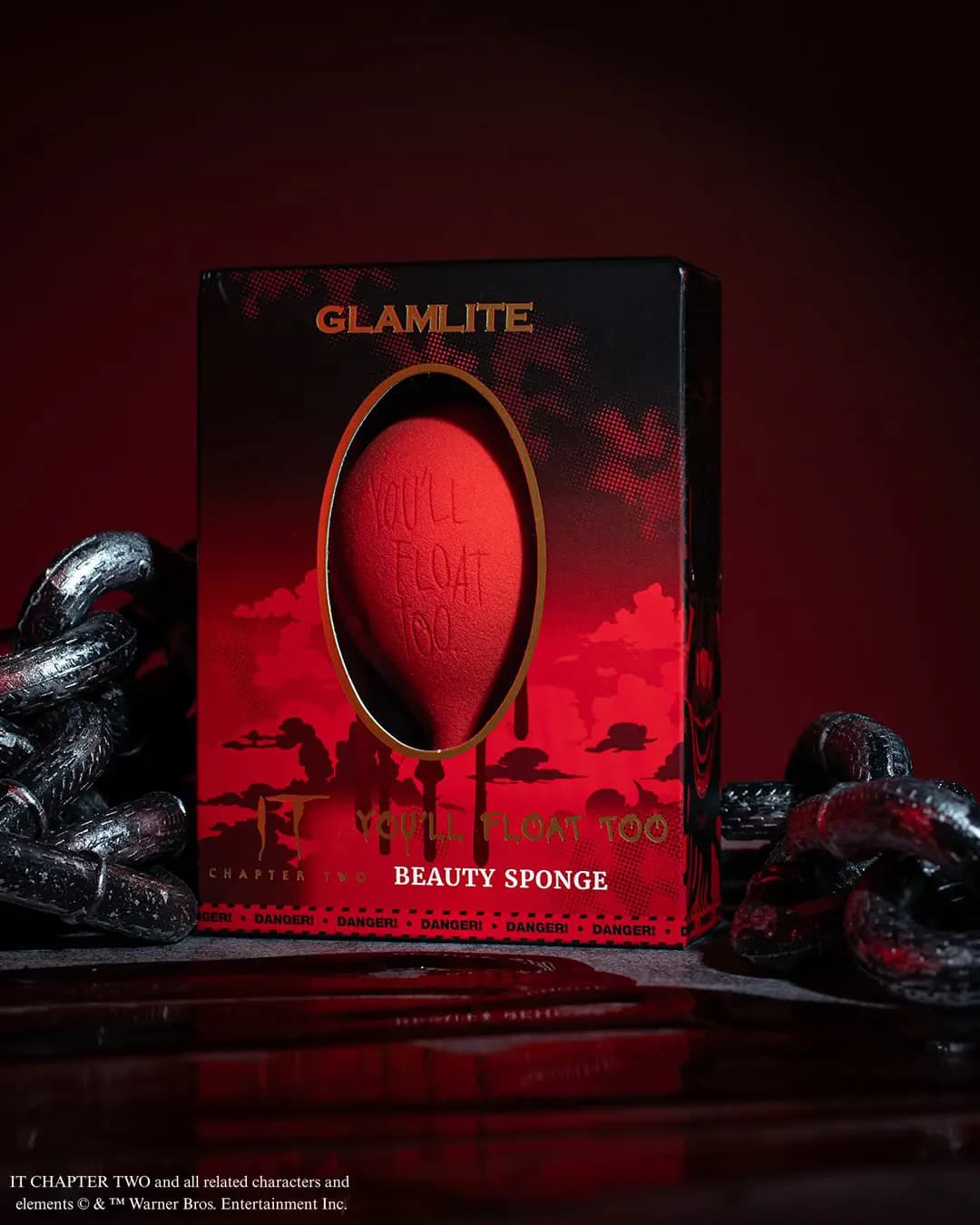 Red balloon-shaped beauty sponge engraved You'll Float Too in a red and black Glamlite box surrounded by chains