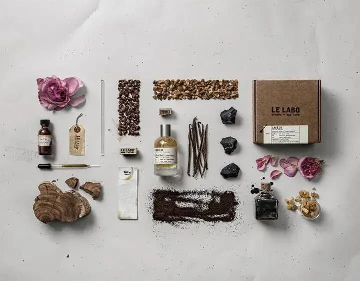 Flat lay of the bottle and kraft Le Labo box with roses, coffee beans, vanilla pods, resin, wood and ground coffee