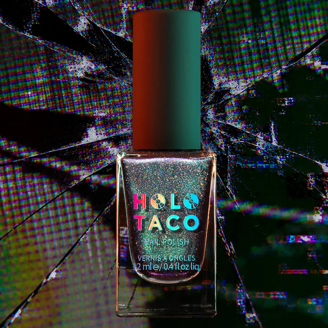 Bottle of smoky purple polish with teal shimmer and holo sparkle against a broken screen backdrop
