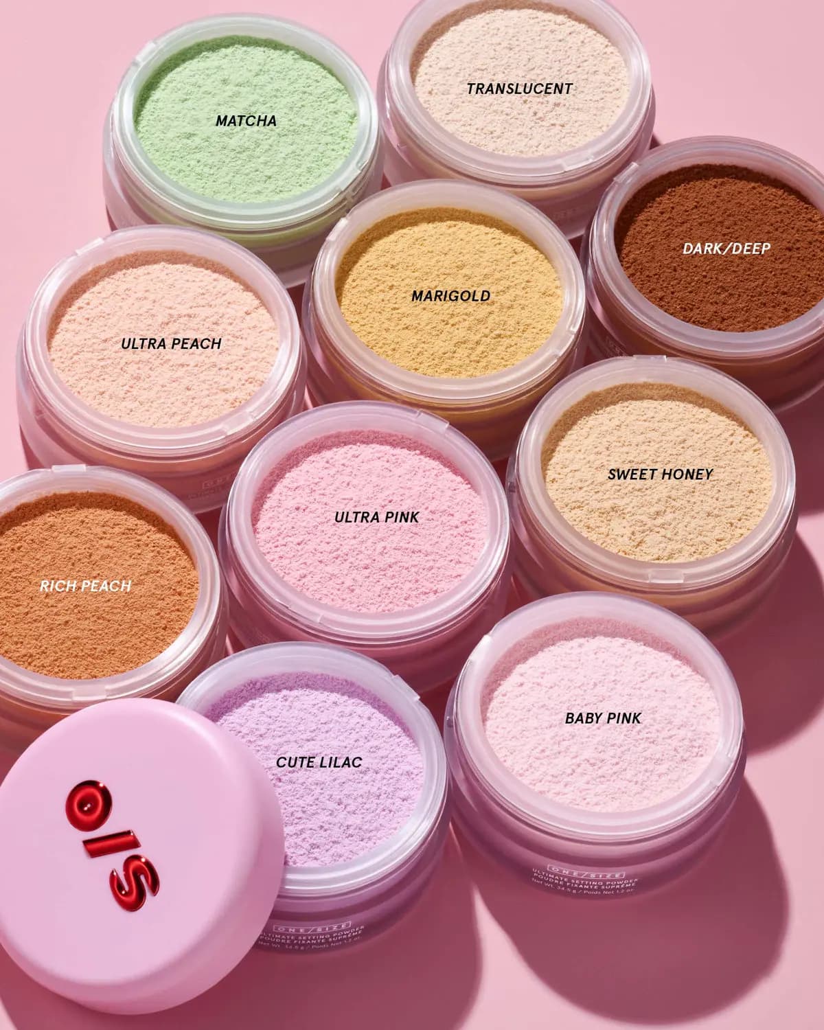 Ten open jars of loose setting powder in labelled shades including Matcha, Cute Lilac and Baby Pink on a pink backdrop