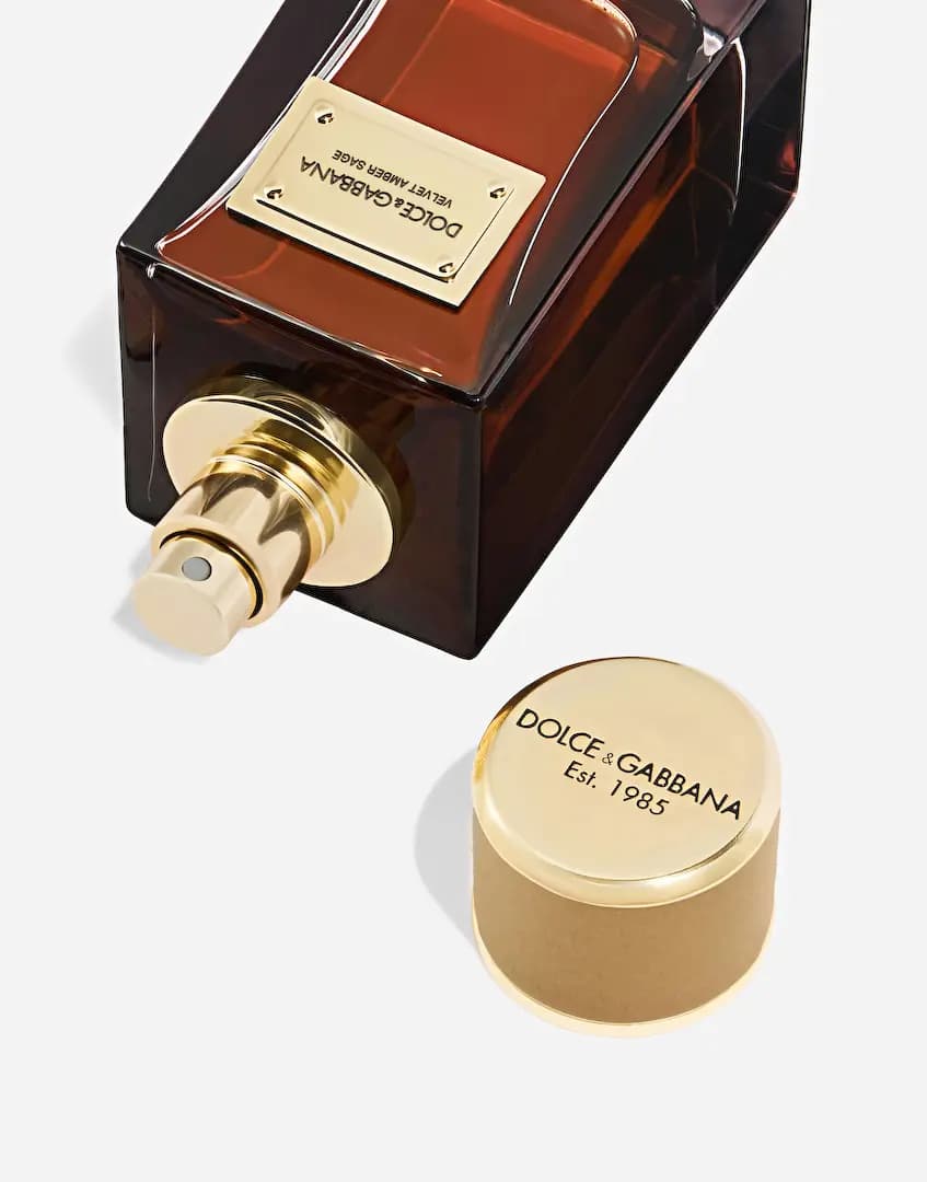 Bottle lying on its side with gold spray nozzle exposed, cap beside it engraved Dolce&Gabbana Est. 1985
