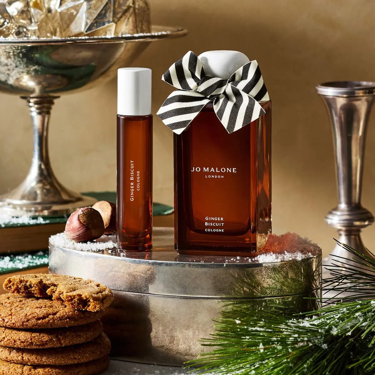 Full-size Ginger Biscuit Cologne and travel spray on a silver tray with gingerbread cookies, pine and ornaments.