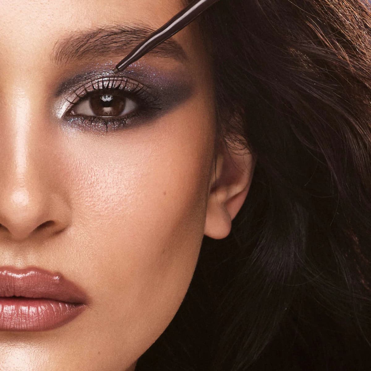 Brown-haired model with silver-violet smoky shadow as a brown pencil touches her eyelid.