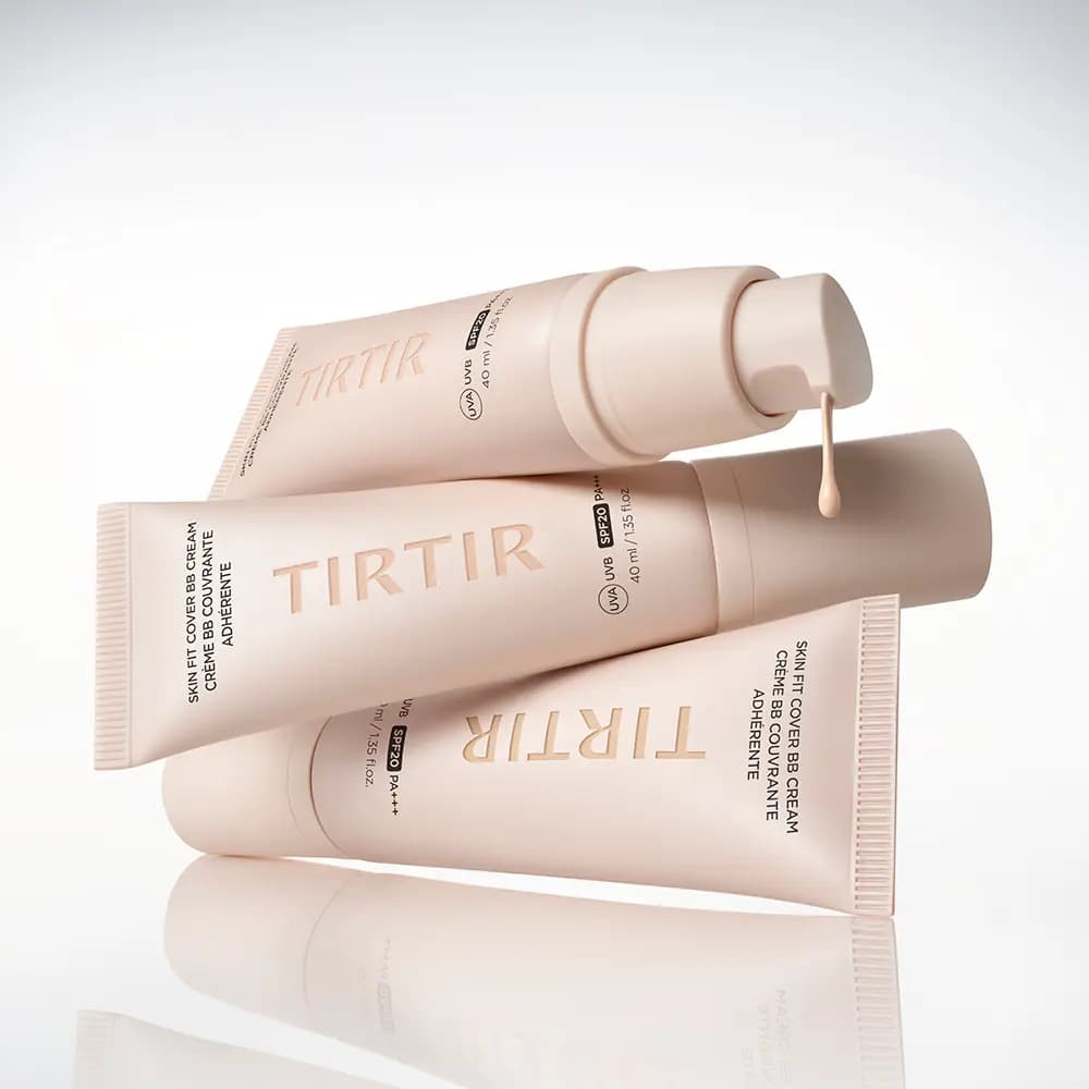 TIRTIR Skin Fit Cover BB Cream tubes in pale pink stacked, one pump dripping a bead of beige cream, on a reflective surface
