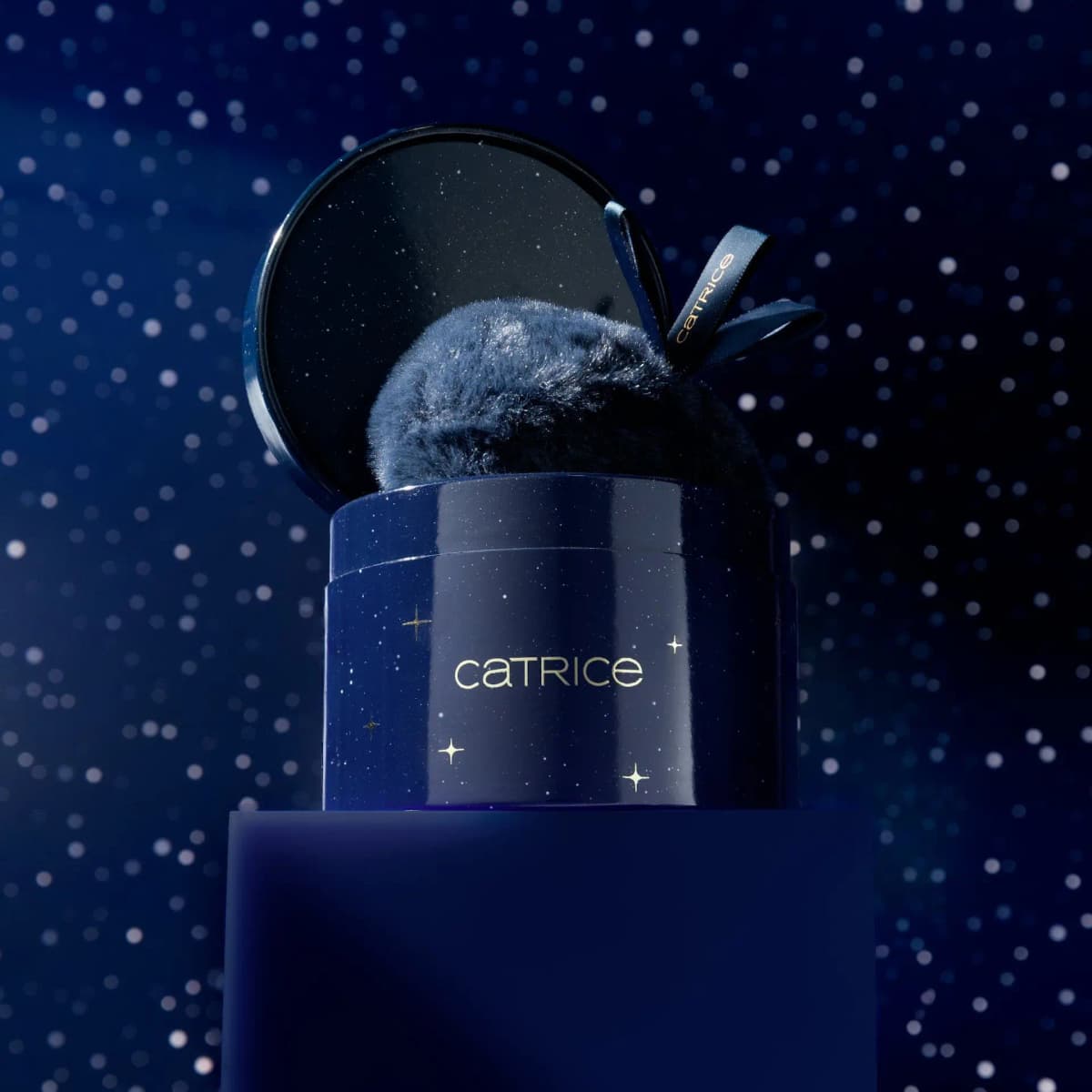 Highlighter box with lid tilted open and a navy fluffy puff peeking out, on a blue plinth under starry sky