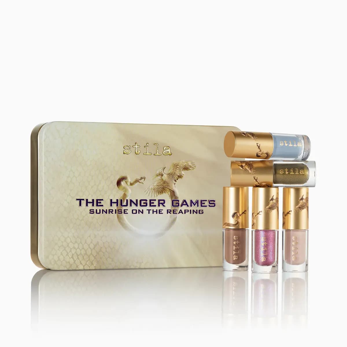 Gold snakeskin-print tin beside five mini liquid shades in blue, olive, taupe, pink sparkle and nude with gold caps