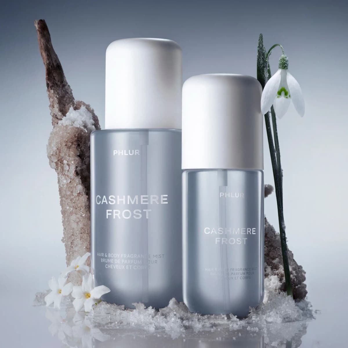 Full-size and travel-size PHLUR Cashmere Frost mists among snow and crystals, with a snowdrop and small white flowers.