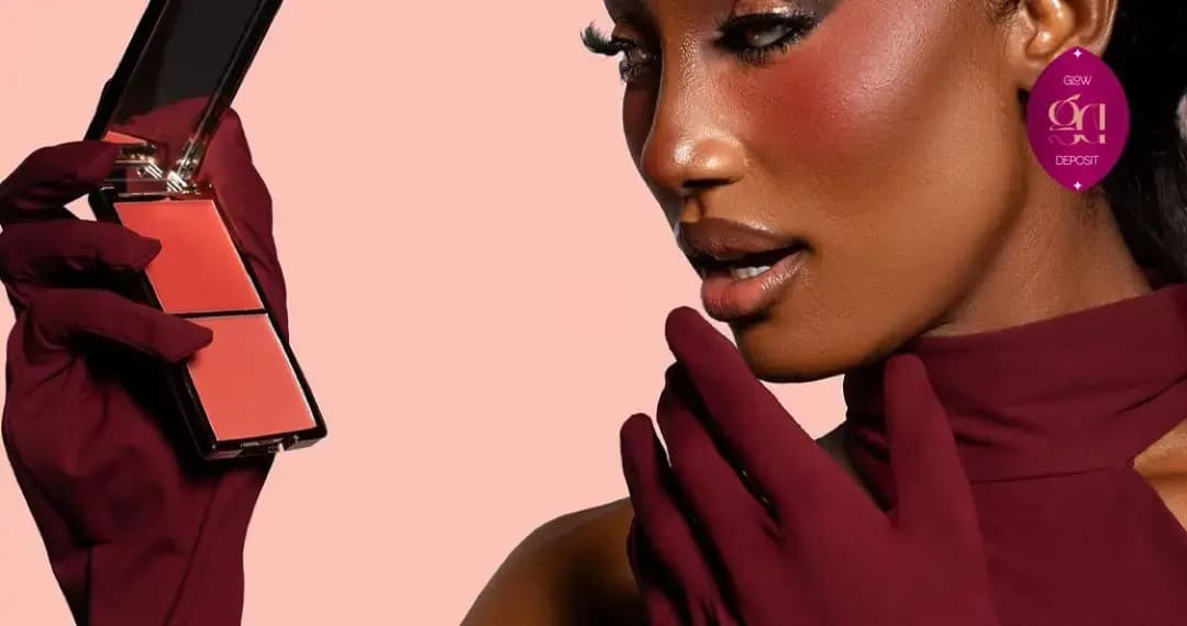 Model in burgundy gloves and top gazes at a coral blush duo, cheeks flushed with warm red-brown blush