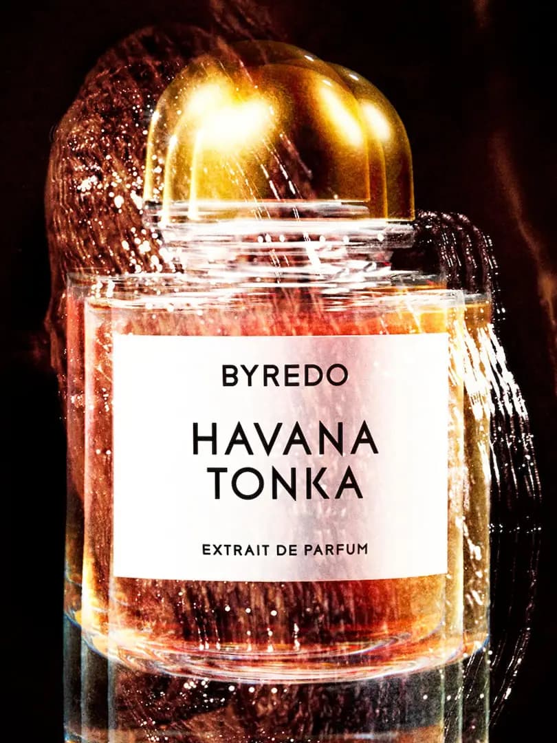 Byredo Havana Tonka Extrait de Parfum bottle with gold cap, blurred with amber light streaks on a dark backdrop