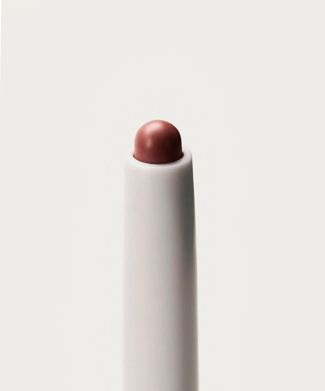 Close-up of a rounded rosy-brown lip liner tip emerging from a white pencil barrel