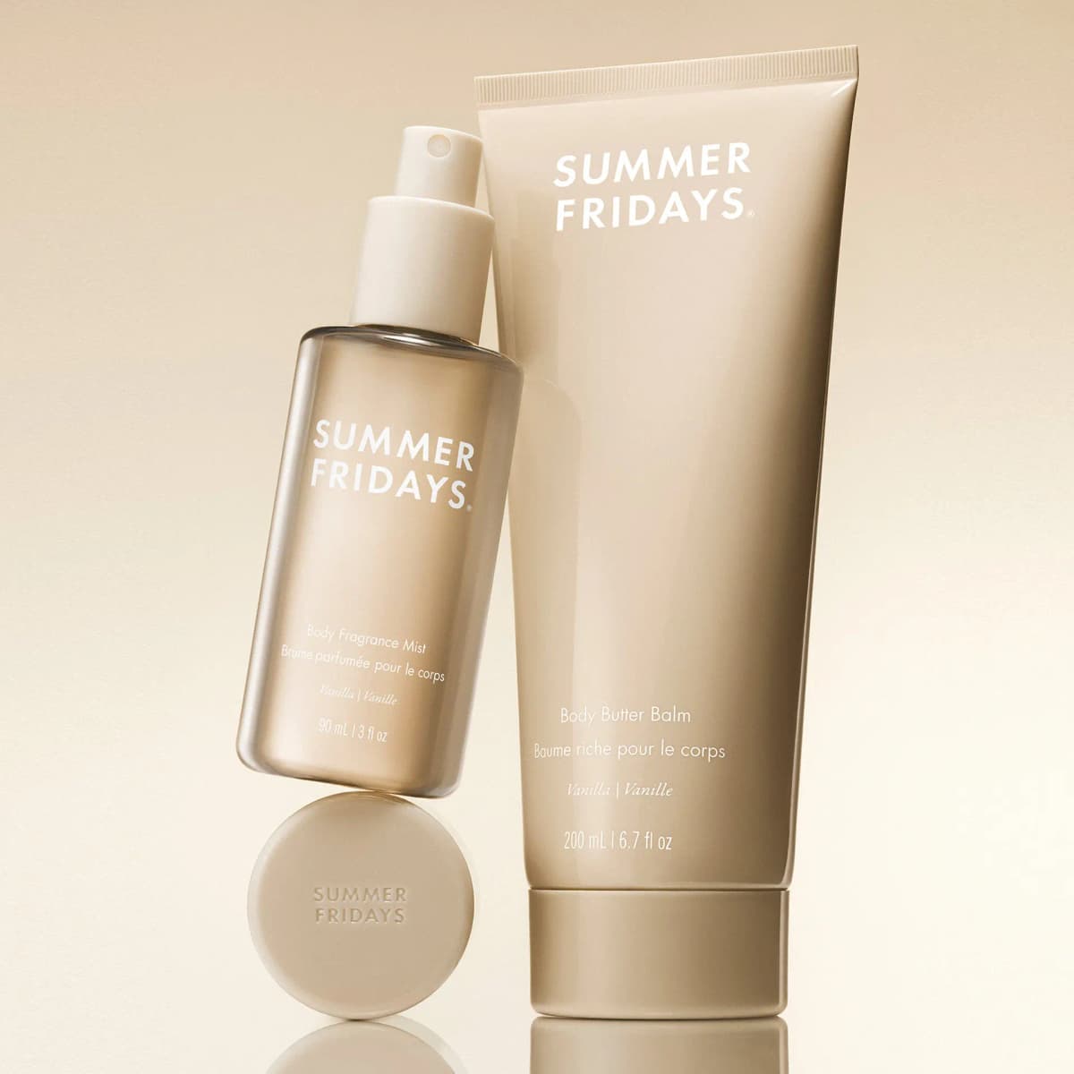 Glossy beige Vanilla Body Fragrance Mist balanced on its cap, leaning against the Body Butter Balm tube on a warm backdrop.
