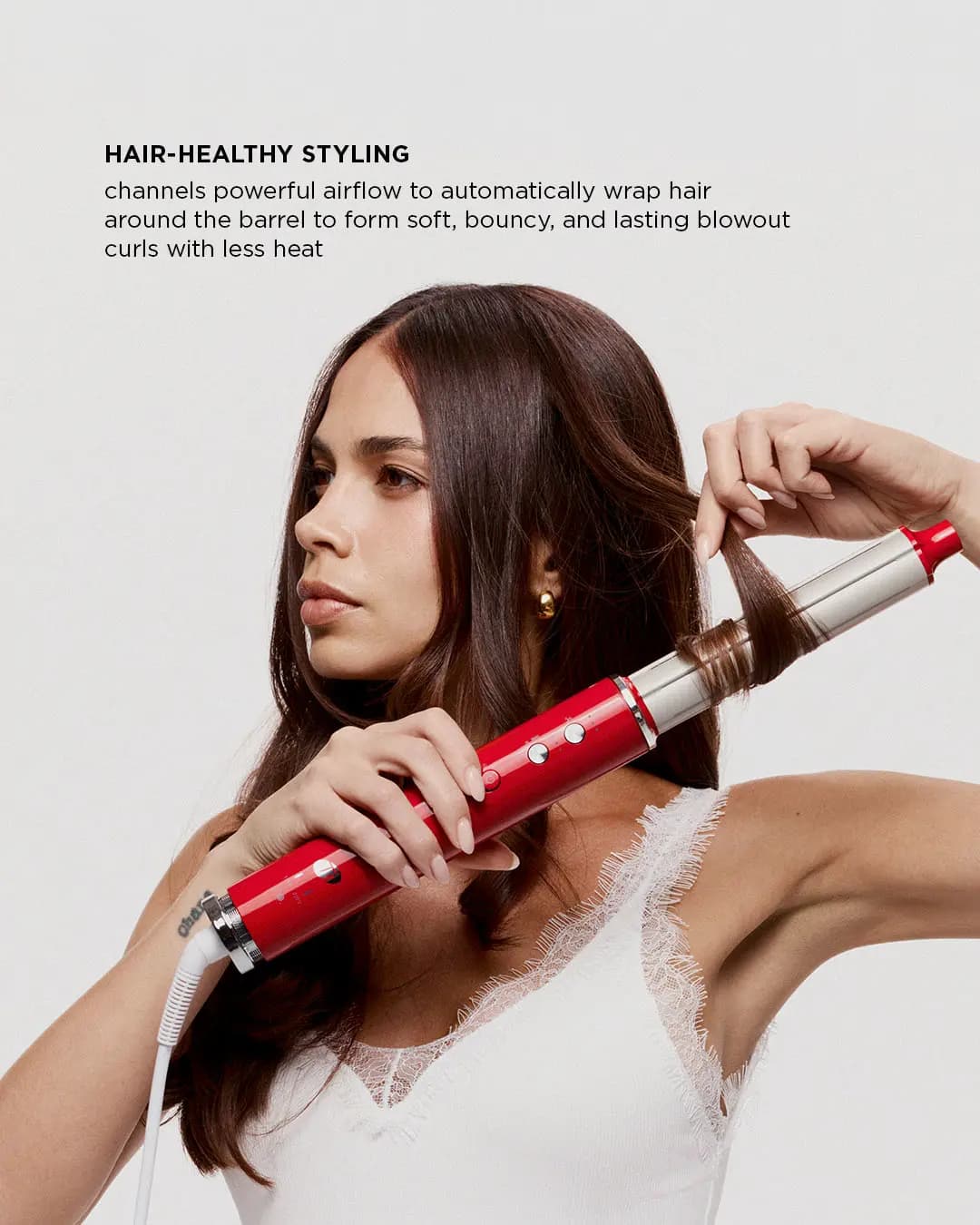 Model wrapping a section of brunette hair around the silver curling barrel, captioned Hair-Healthy Styling