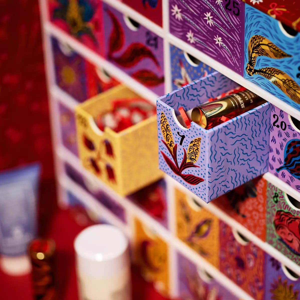 Lilac drawer 7 with yellow leaf motif slid open to reveal a gold Supremÿa tube among red paper shreds