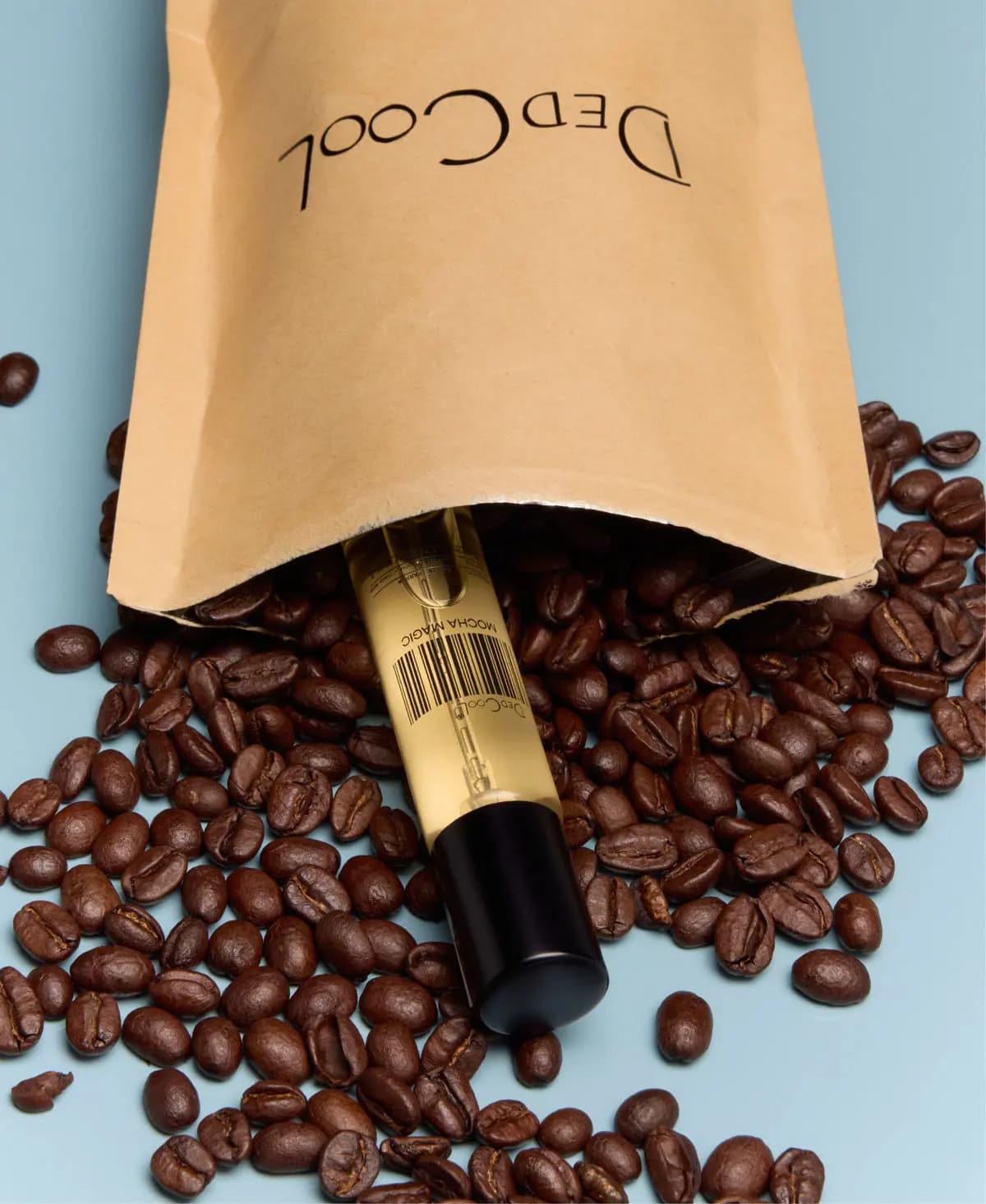 DedCool travel-size Mocha Magic bottle spilling from a kraft paper bag onto scattered coffee beans