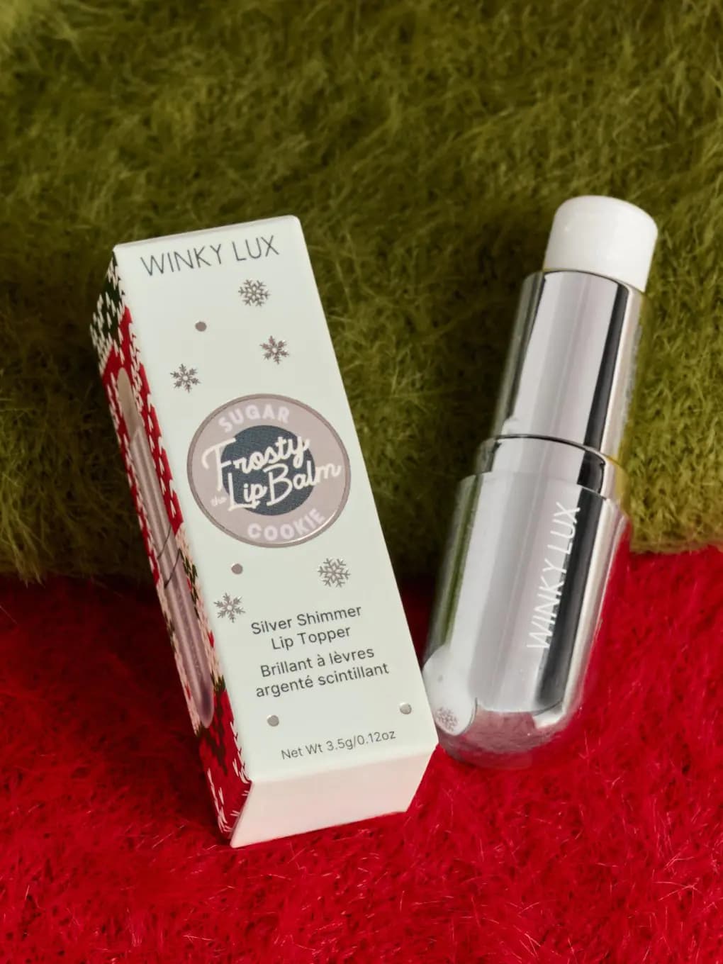 Frosty the Lip Balm box in Sugar Cookie with snowflakes beside the silver tube on green and red knit fabric