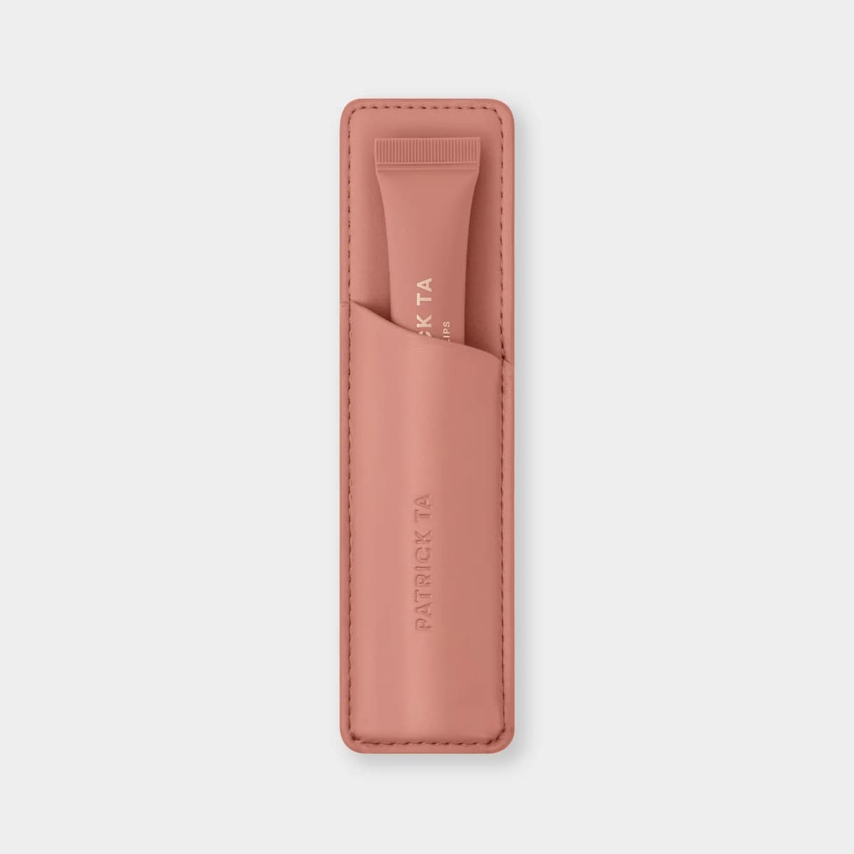 Peachy-pink leather sleeve with debossed Patrick Ta logo and a matching lip balm tube tucked into its slanted pocket