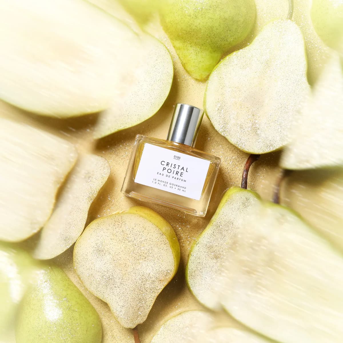 Bottle lying among sliced pears dusted with gold glitter on a pale yellow surface