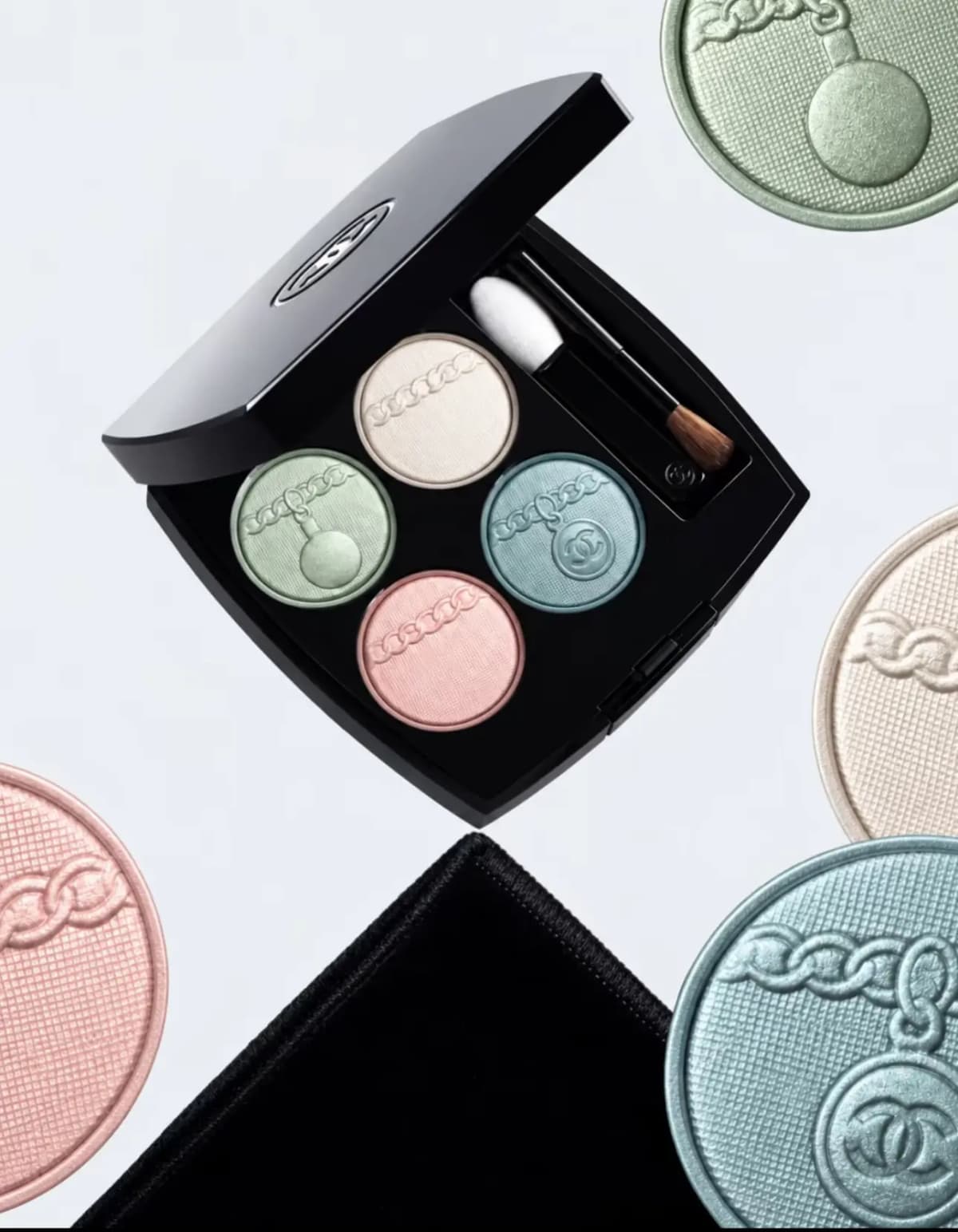 Open black lacquered Chanel square compact holding four pastel eyeshadow pans in mint, ivory, powder blue and pink.