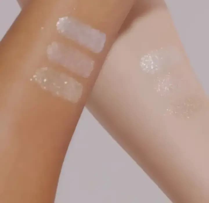 Three sparkling glitter swatches on a deep skin tone arm beside sheer shimmering swatches on a fair arm