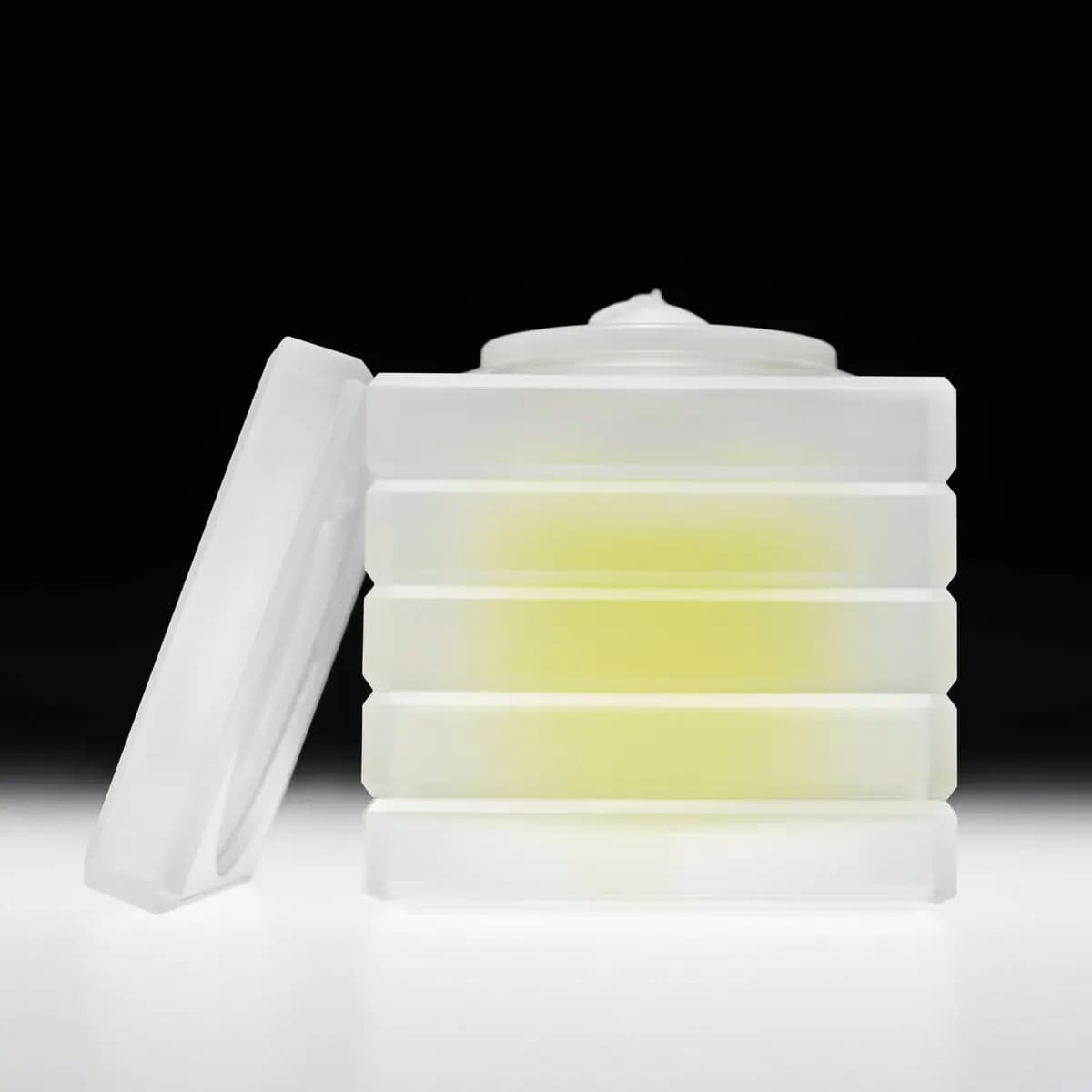 Frosted ridged case glowing yellow from within, gel dispensed on the pump, lid leaning beside, on black backdrop
