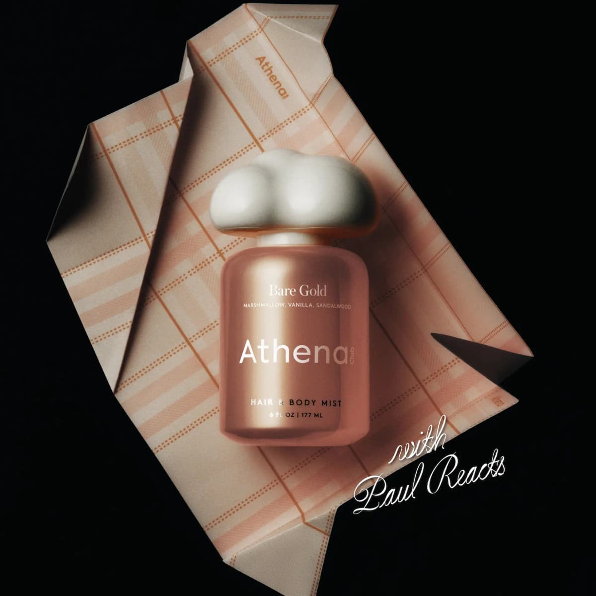 Peach mist bottle with a white cloud-shaped cap lying on folded plaid Athena wrapping paper against black