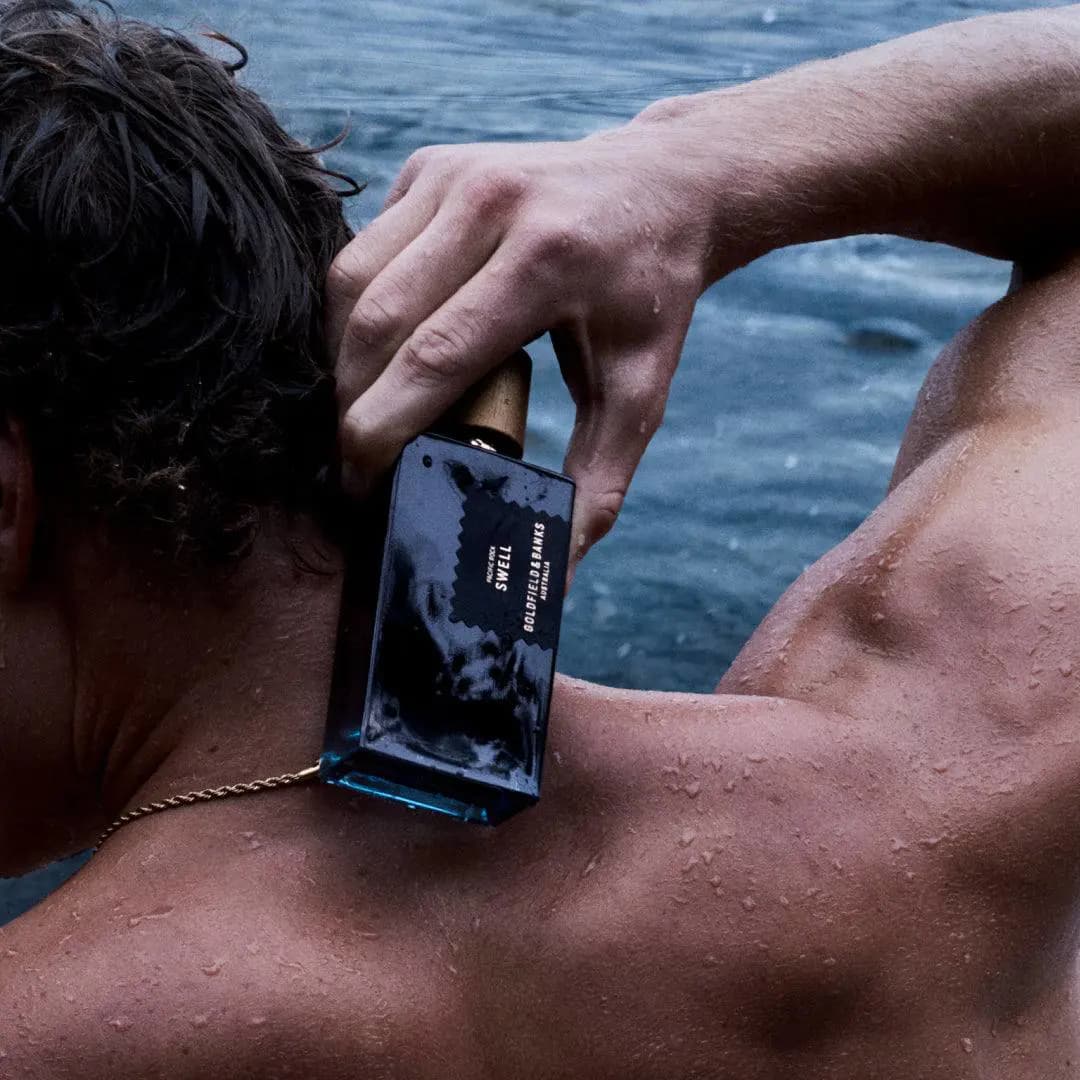 Wet bottle of Pacific Rock Swell pressed against a man's neck and shoulder with the sea behind