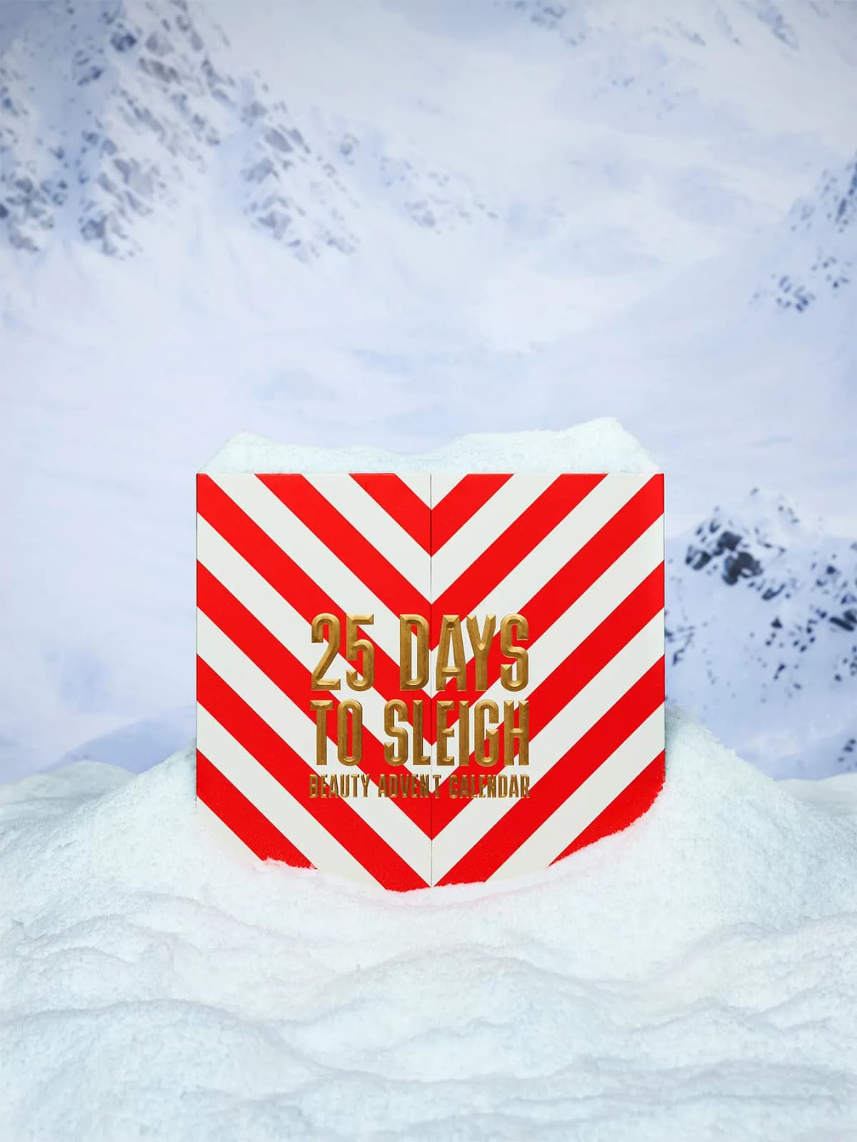 Red and white chevron-striped 25 Days to Sleigh beauty advent calendar box set in snow before snowy mountains