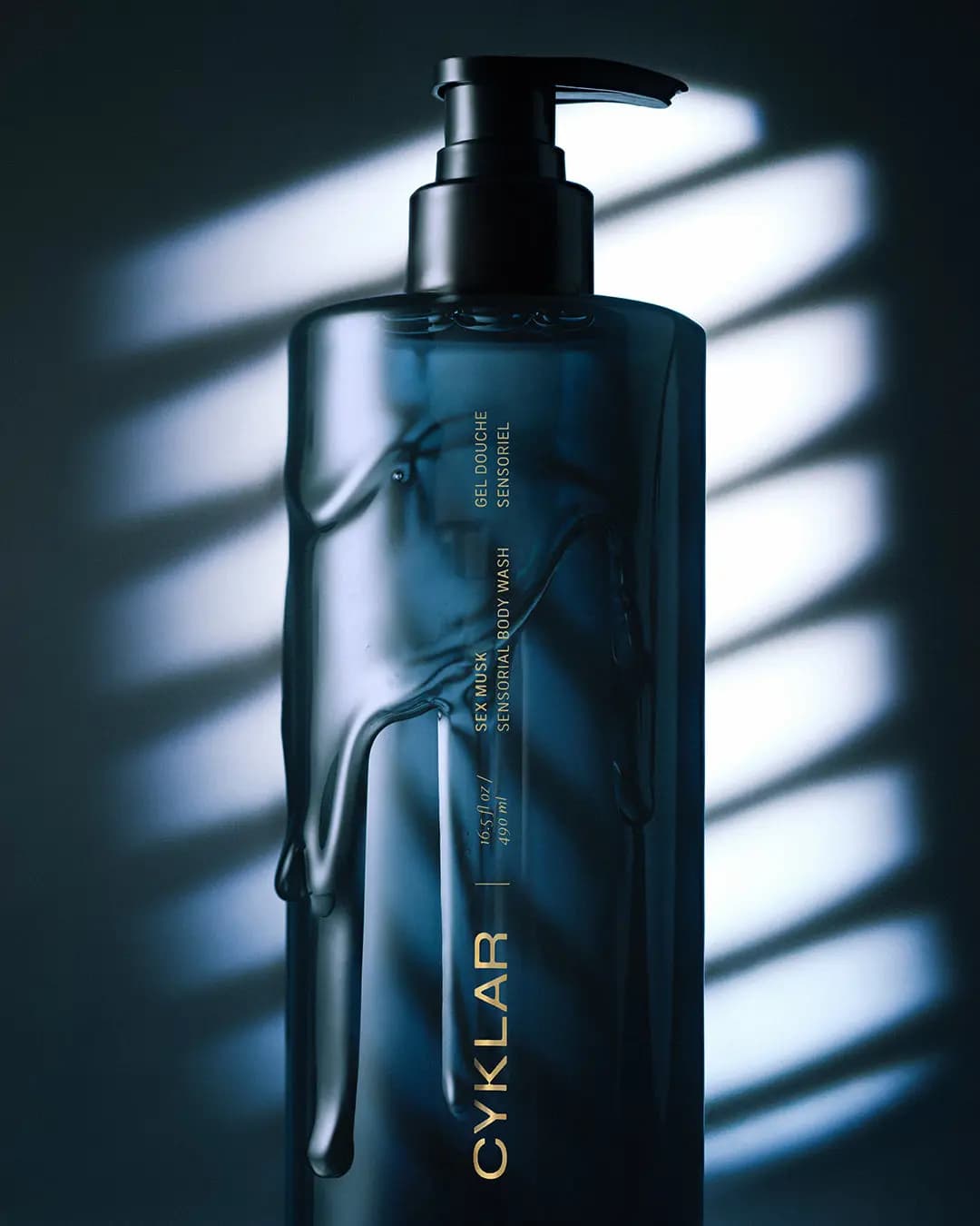 Body wash bottle with clear gel dripping down its sides, lit by blue light and slatted window shadows
