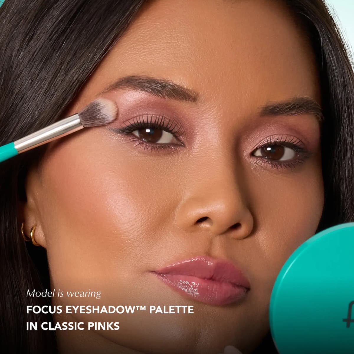 Model with brown eyes blending rosy-mauve shadow on her lid with a teal-handled brush, wearing Classic Pinks.