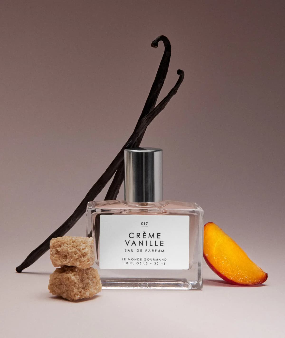 Crème Vanille bottle posed with vanilla pods, brown sugar cubes and an apricot slice against a mauve backdrop