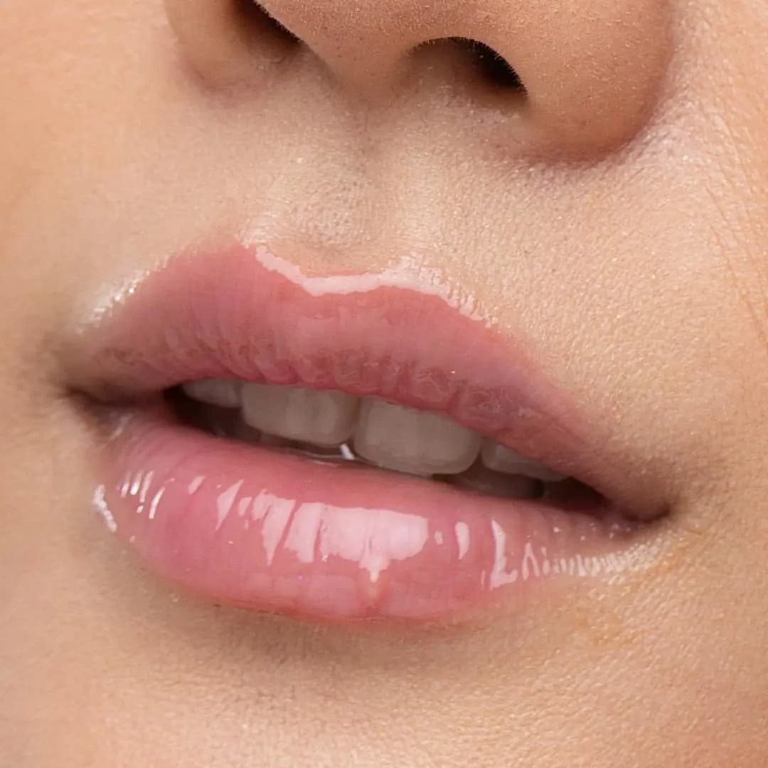 Close-up of glossy lips wearing a sheer pink, high-shine lip oil.