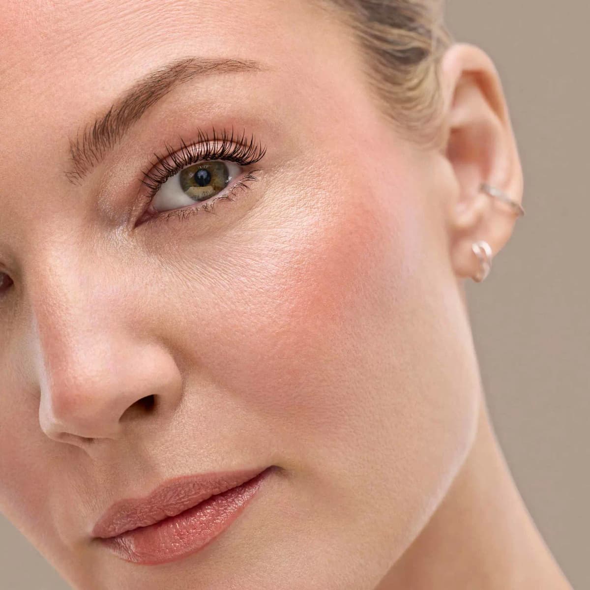 Close-up of a model with a glowing peachy flush on the cheek, highlighted cheekbone and glossy nude lip