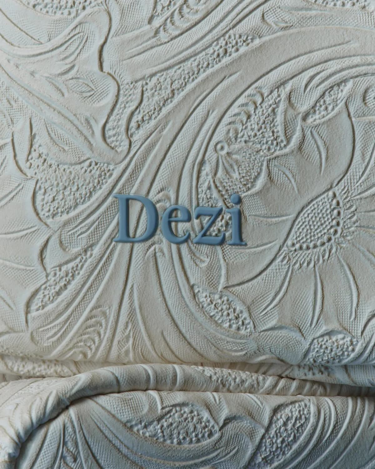 Close-up of the cream bag's embossed floral heritage print with a raised blue Dezi logo