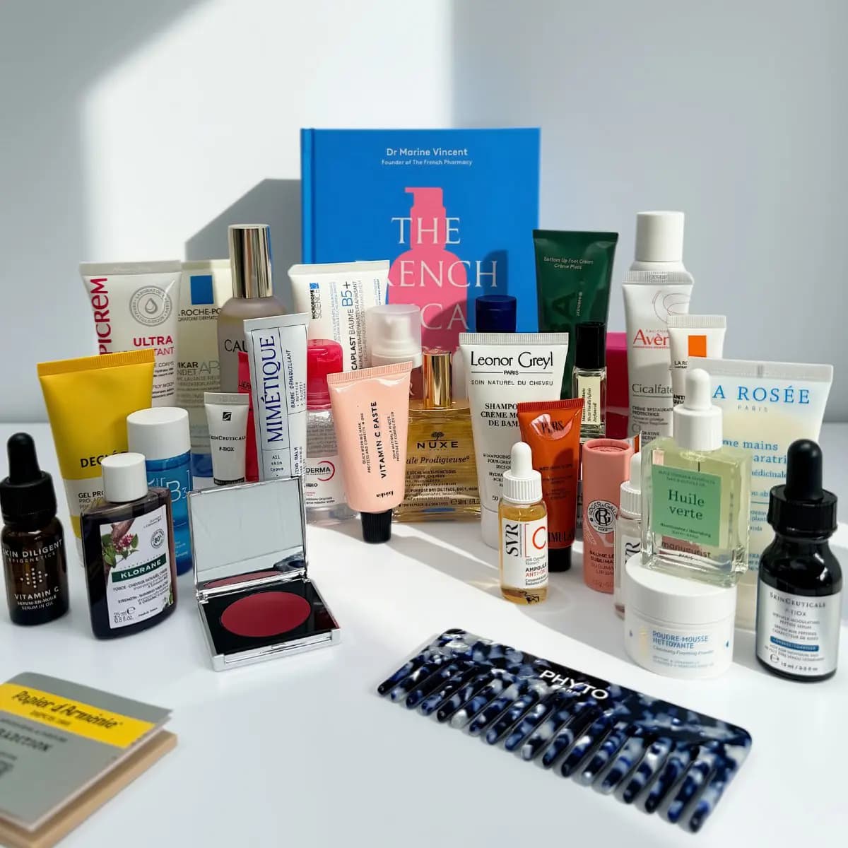 Array of French pharmacy skincare, haircare and beauty products arranged around a blue book titled The French Skincare Bible